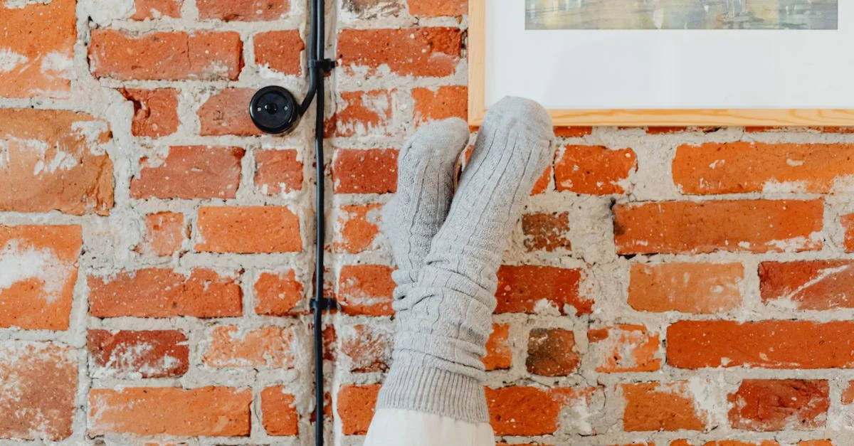 Des chaussettes grises reposent contre un mur en brique rustique, créant une atmosphère intérieure conviviale.