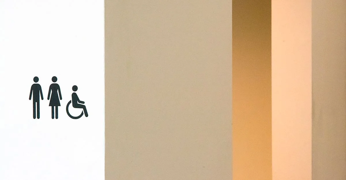 Panneau de toilettes minimaliste avec des symboles masculin, féminin et de fauteuil roulant sur un mur moderne.