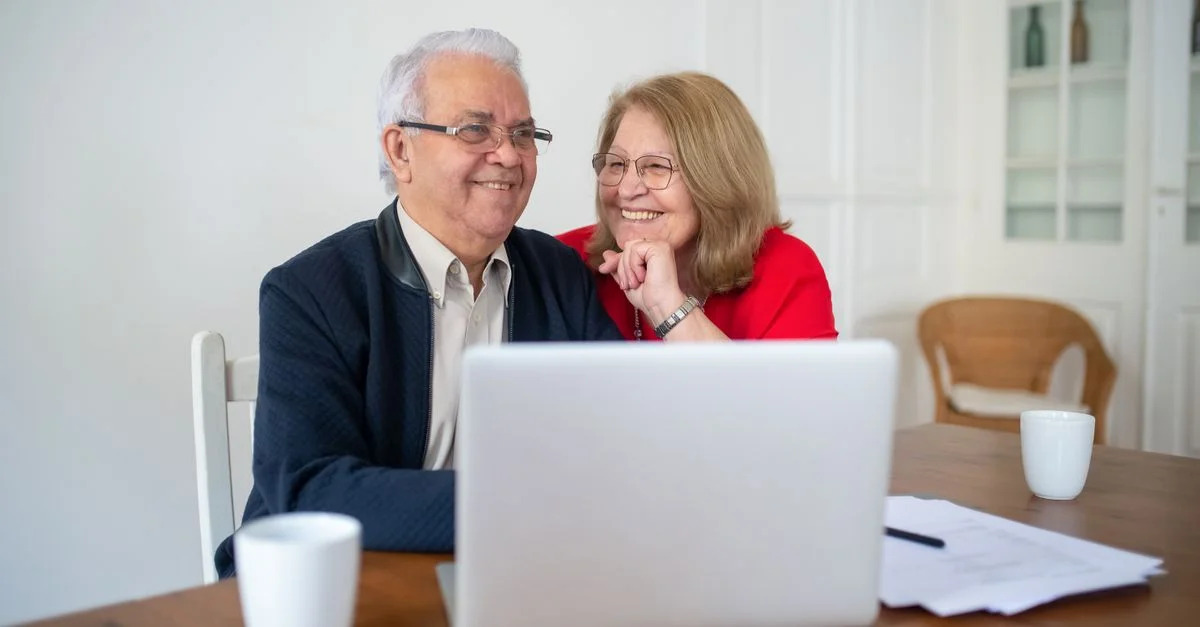 Couple senior souriant en utilisant un ordinateur portable à la maison, profitant d'activités en ligne ensemble.