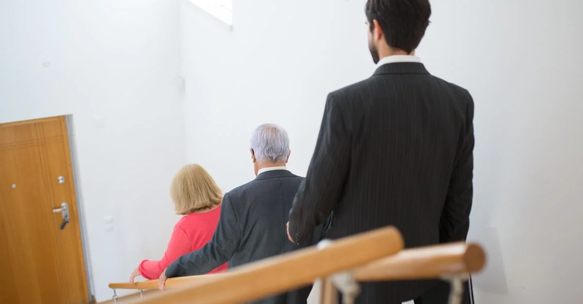 Un couple senior et un jeune homme en costumes descendant un escalier moderne à l'intérieur.