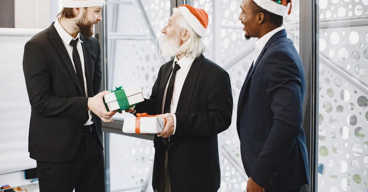 Trois hommes d'affaires en chapeaux de Santa échangeant des cadeaux dans un bureau festif.