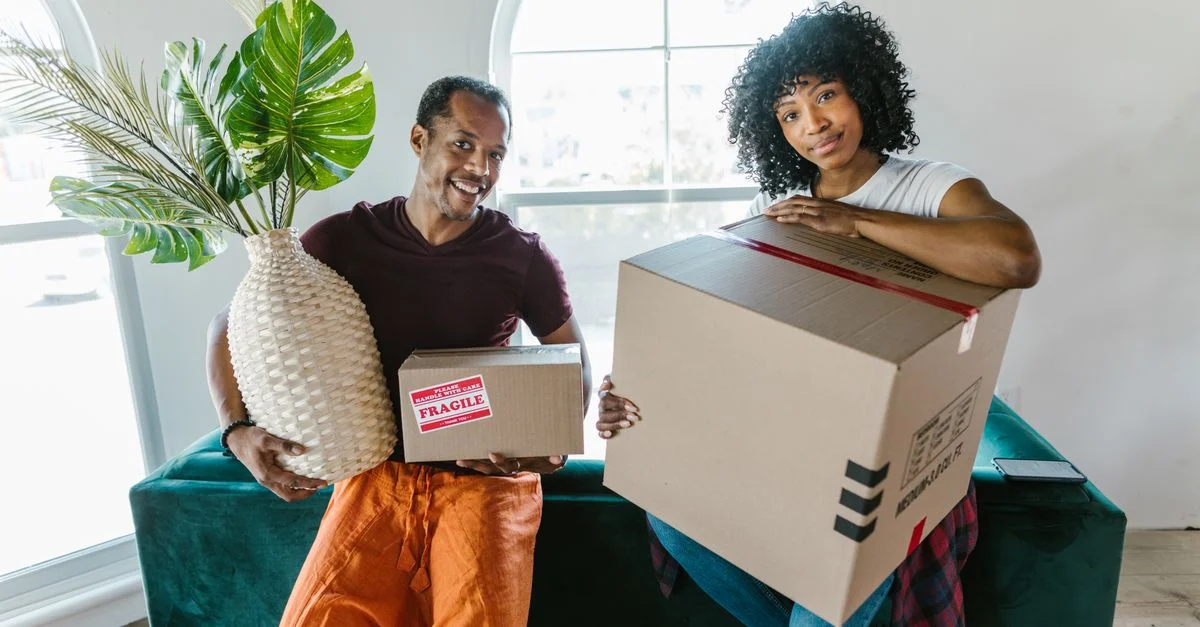Un couple joyeux emménage dans leur nouvelle maison, tenant des cartons et souriant.