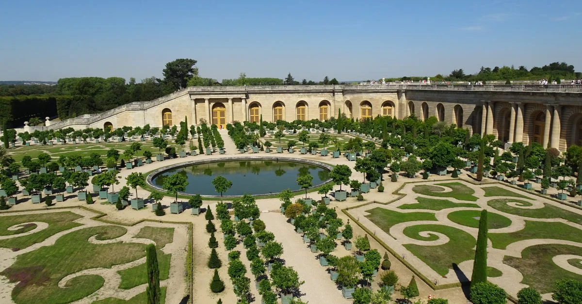 Vue aérienne des jardins emblématiques du château de Versailles, mettant en valeur un aménagement paysager raffiné et une architecture classique.