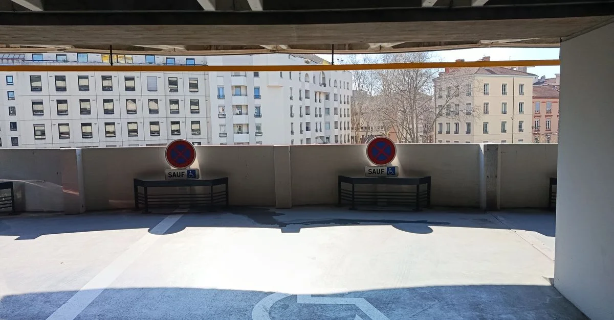Un niveau de parking souterrain vide, avec des panneaux de stationnement pour personnes handicapées visibles et des panneaux d'interdiction de stationner à l'extérieur des bâtiments municipaux.