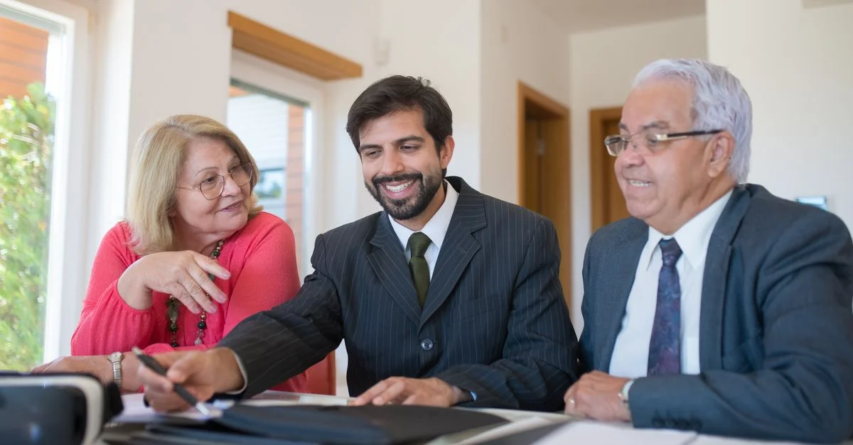 Agent immobilier professionnel discutant d'une transaction immobilière avec un couple senior dans un bureau lumineux.