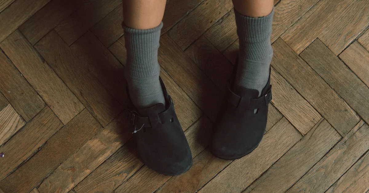Gros plan sur une personne portant des sandales noires avec des chaussettes bleues sur un sol en parquet en bois.