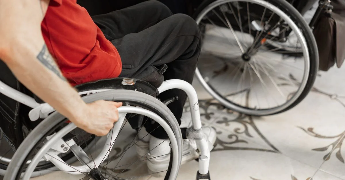 Gros plan d'une personne dans un fauteuil roulant portant une chemise rouge, à l'intérieur.