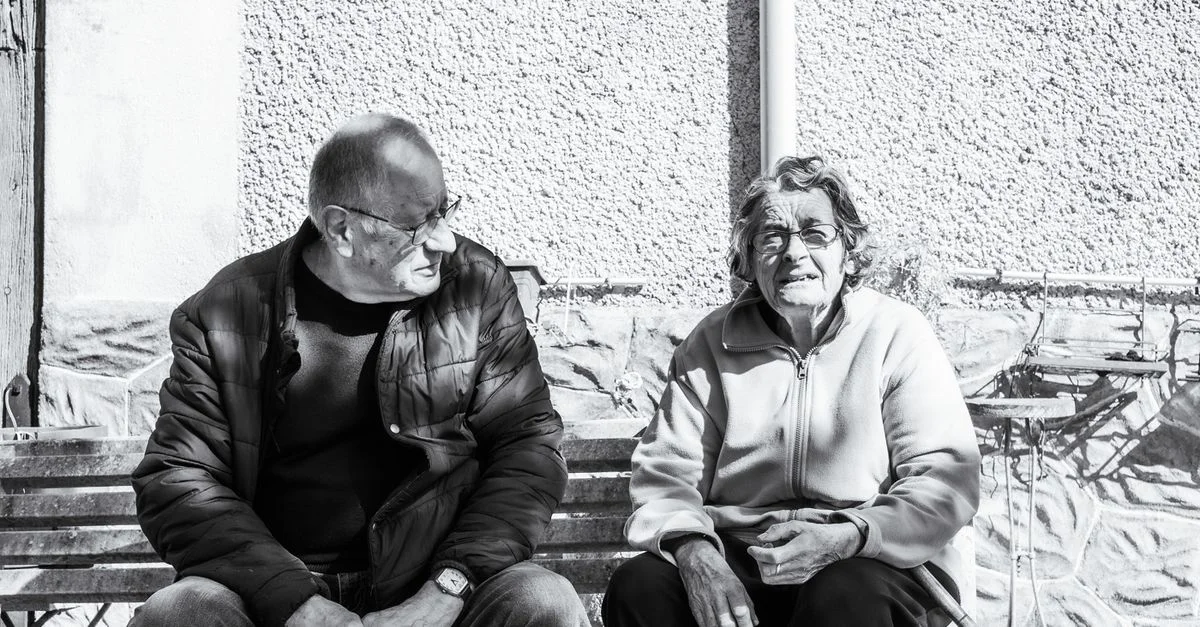 Portrait en noir et blanc d'un couple âgé assis sur un banc à Parcoul-Chenaud, France.