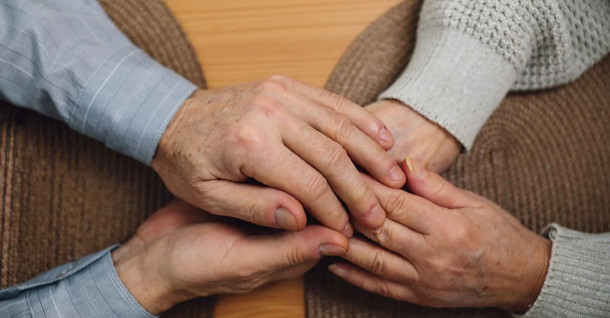 Gros plan de mains âgées se tenant sur une table en bois, symbolisant l'amour et la connexion.