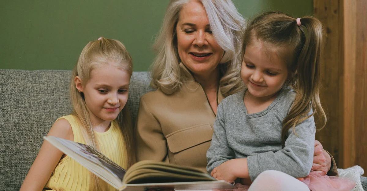 Grand-mère lisant un livre avec deux petites-filles, créant un moment familial chaleureux.
