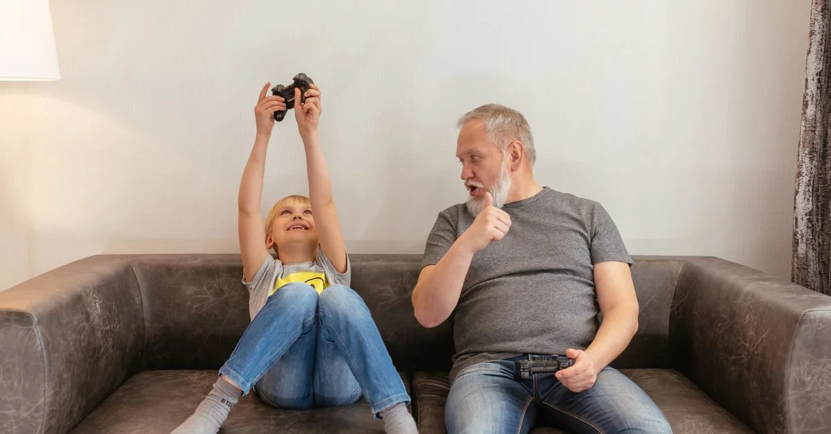 Un grand-père et son petit-fils partagent des moments amusants à jouer à des jeux vidéo sur un canapé.