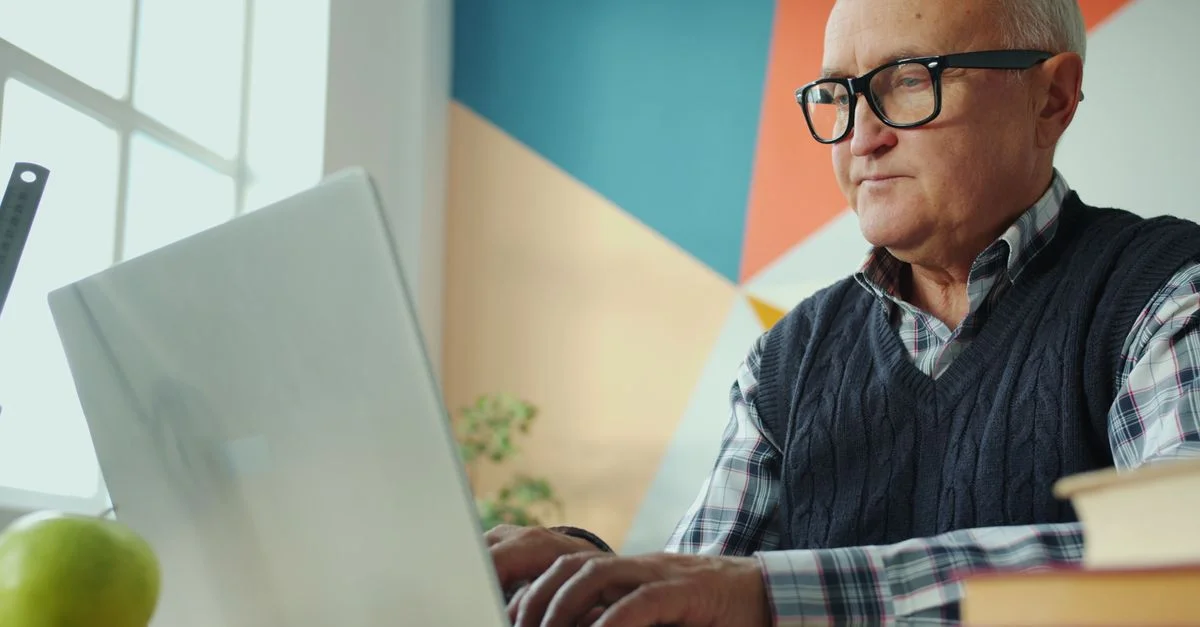Homme âgé concentré sur son ordinateur portable dans un environnement de bureau élégant et coloré.