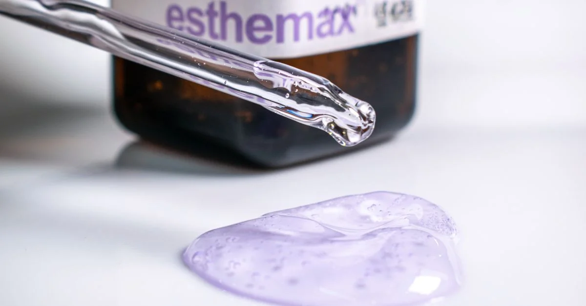 Gros plan sur un gel de soin de couleur violette et une pipette avec une bouteille Esthemax, mettant en avant les composants clés des soins de la peau.