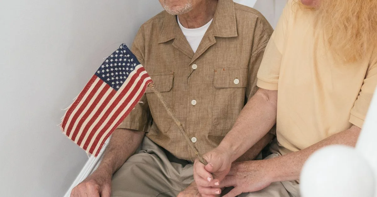 Un couple senior assis sur des escaliers à l'intérieur, tenant ensemble un petit drapeau des États-Unis.