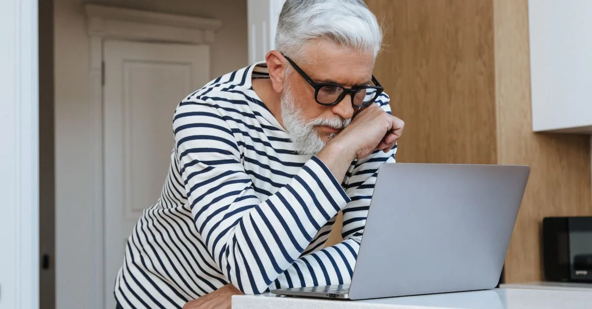 Un homme senior avec des lunettes se concentrant sur son ordinateur portable à domicile, symbolisant les environnements de travail modernes.