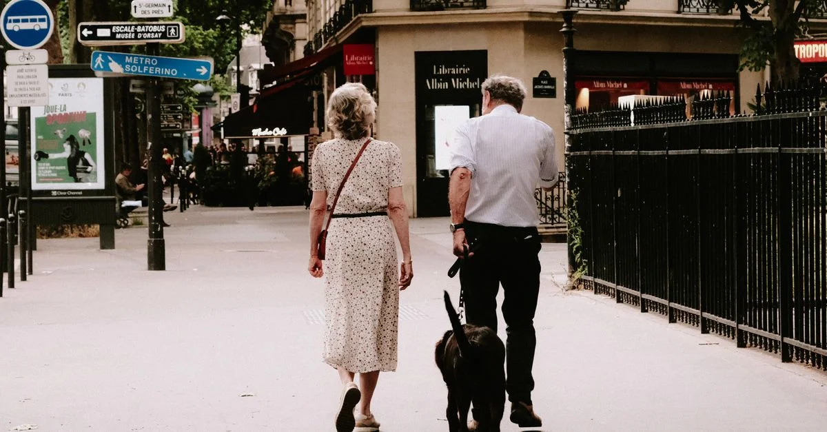 Un couple âgé promenant leur chien dans une charmante rue de Paris, mettant en valeur un après-midi paisible.