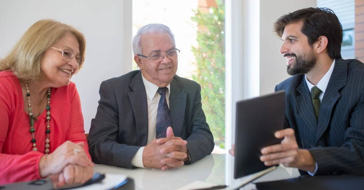 Couple âgé discutant des options immobilières avec un agent dans un cadre de bureau moderne.