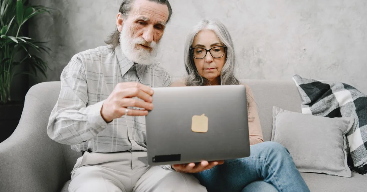 Couple senior utilisant un ordinateur portable à la maison, mettant en avant l'utilisation de la technologie parmi les personnes âgées.