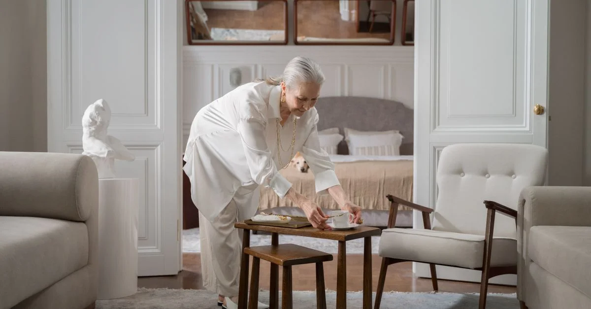 Femme senior préparant le petit-déjeuner sur une petite table dans une pièce élégamment décorée.
