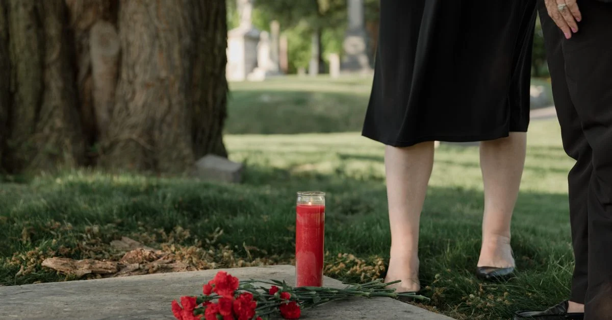 Une scène solennelle dans un cimetière avec une bougie rouge et des fleurs, symbolisant le souvenir.