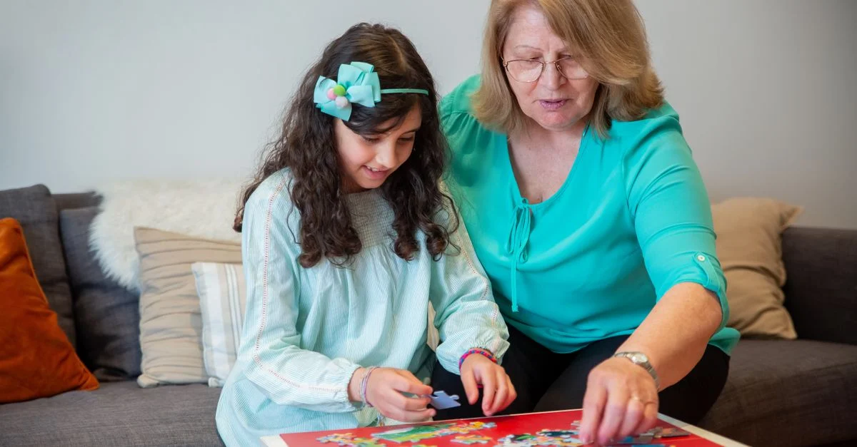 Une grand-mère et sa petite-fille profitent d'un moment de complicité en résolvant ensemble un puzzle.