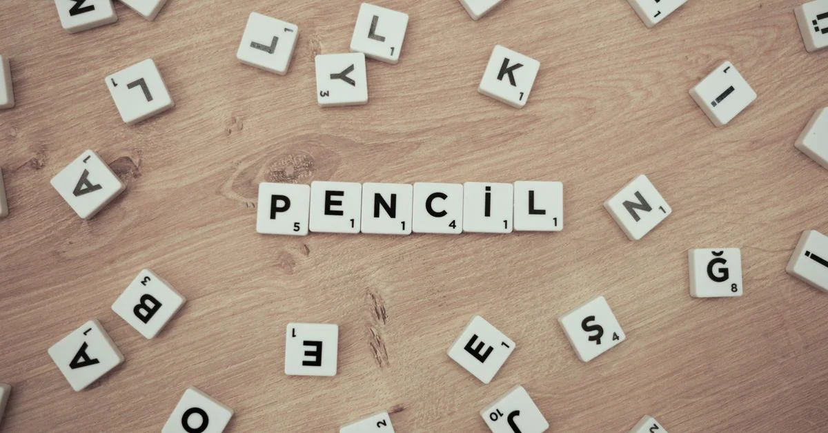 Surface en bois avec des jetons de Scrabble éparpillés formant le mot 'Crayon'.