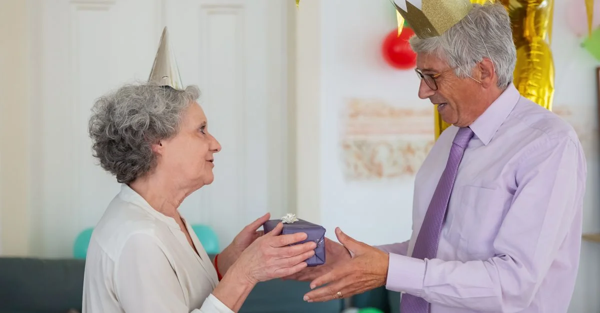 Couple senior heureux échangeant des cadeaux lors d'une célébration d'anniversaire à domicile.