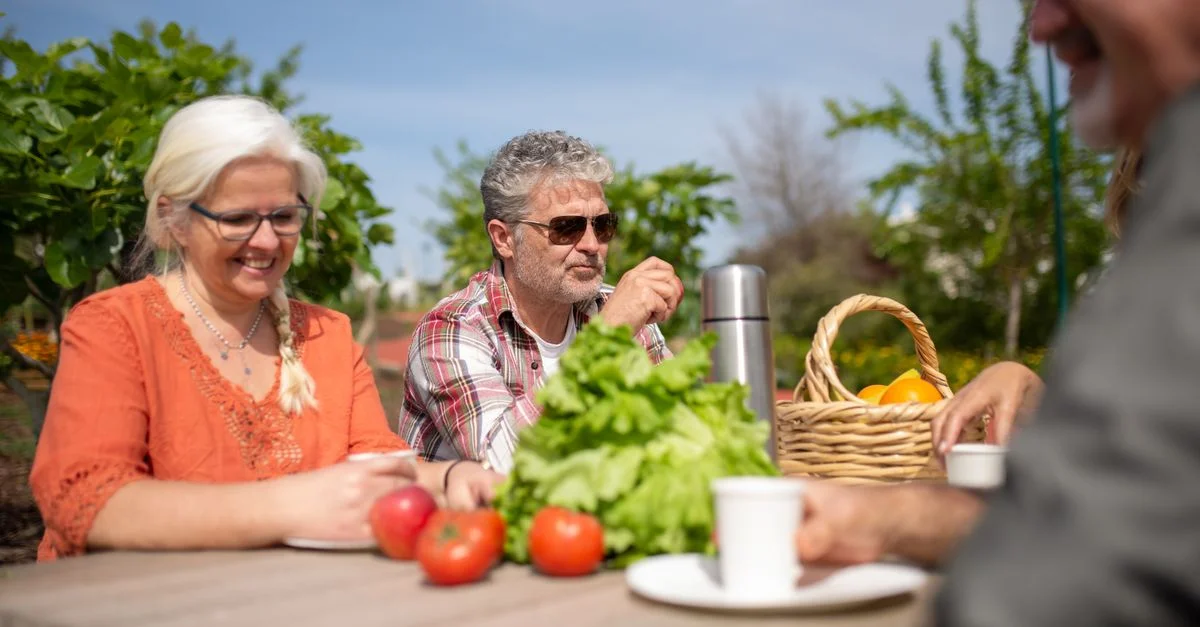 Un groupe d'amis seniors profitant d'un déjeuner décontracté en plein air avec des légumes frais.