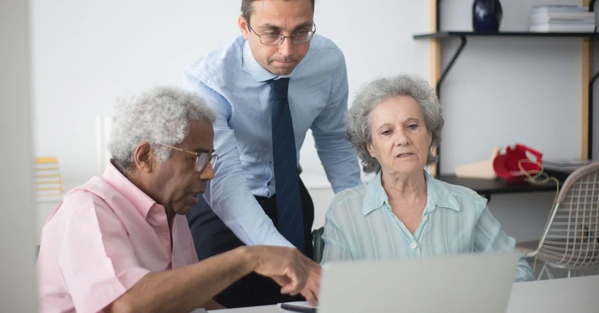 Un couple de seniors consultant un agent commercial à domicile sur un ordinateur portable.