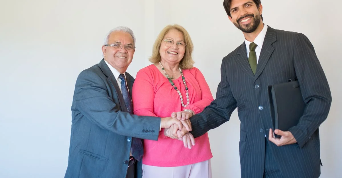 Un couple senior souriant rencontrant un agent immobilier à l'intérieur, signifiant un accord réussi.