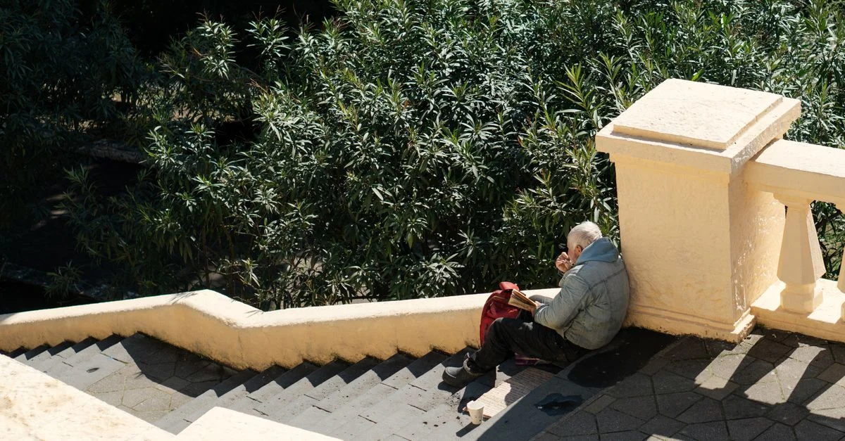 Un homme senior est assis sur les marches en lisant un livre dans la solitude, entouré de verdure.