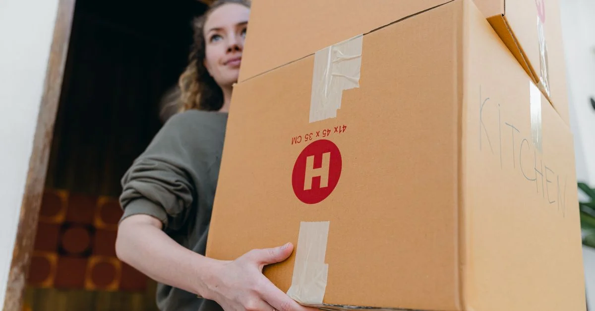 Femme jeune et confiante portant des cartons lors d'un jour de déménagement.