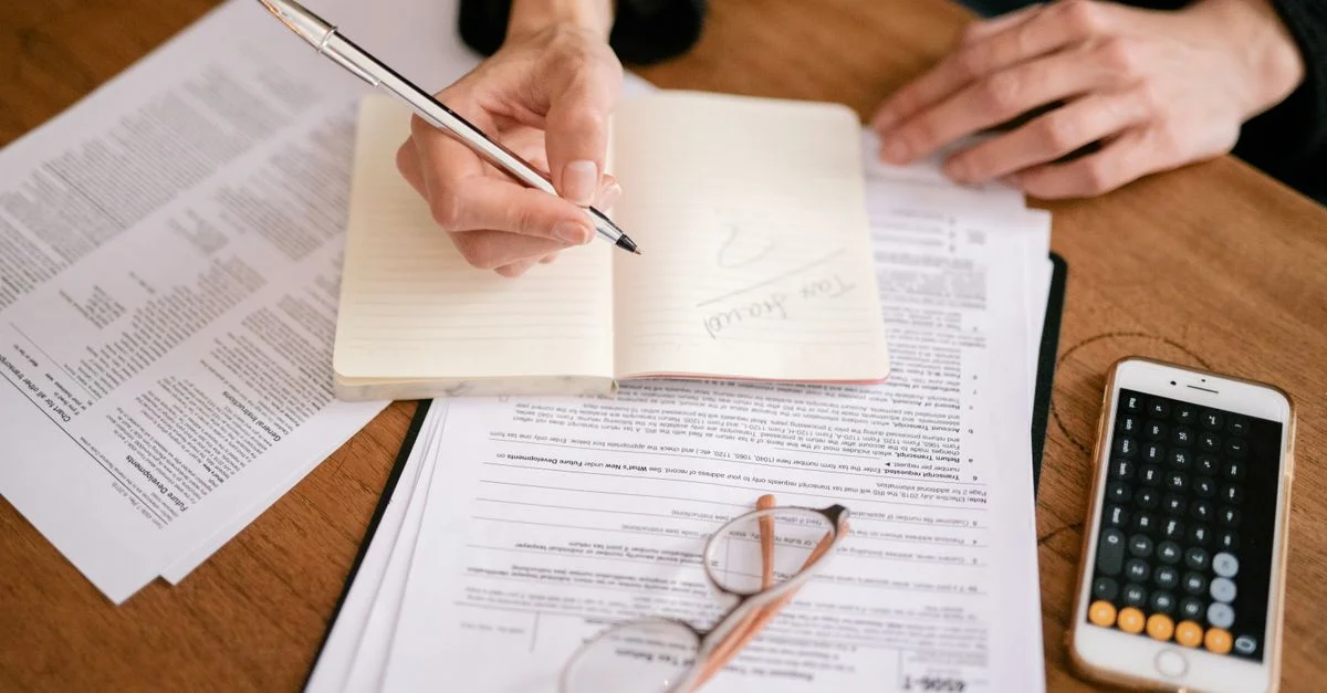 Gros plan d'une personne écrivant dans un carnet avec des documents et une calculatrice, gérant des finances.