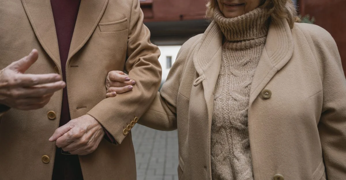 Un couple senior marchant bras dessus bras dessous, portant des manteaux d'hiver confortables. Affection chaleureuse en plein air.