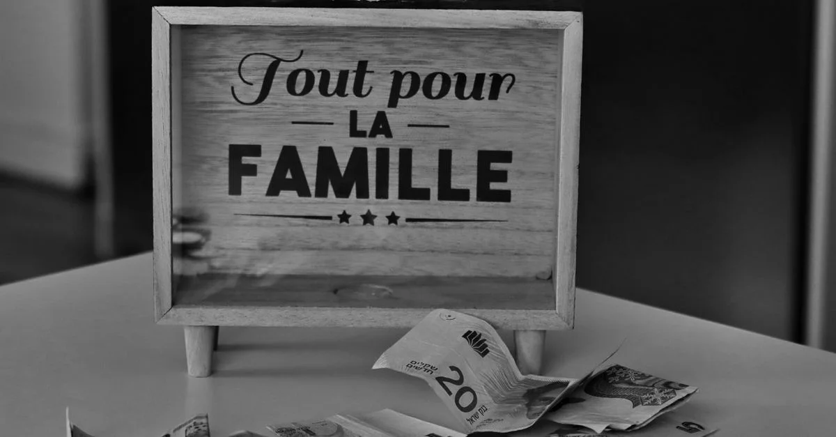 Photo en noir et blanc d'une tirelire et de différentes devises sur une table, symbolisant l'épargne pour la famille.