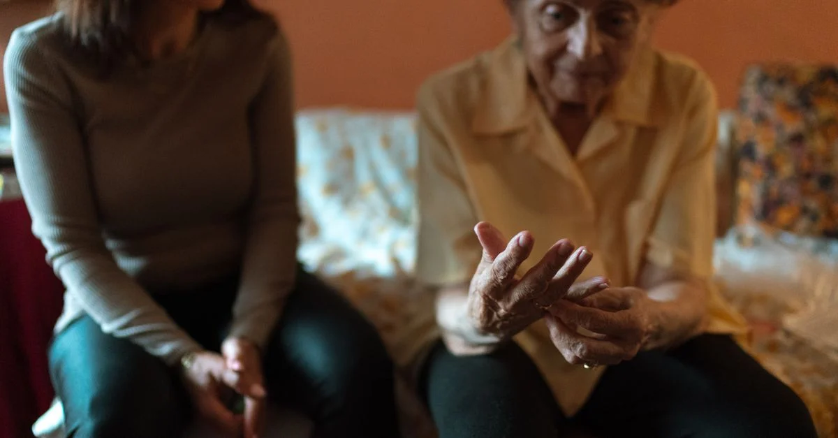 Une femme âgée et son soignant partagent un moment sur le canapé, incarnant la camaraderie.