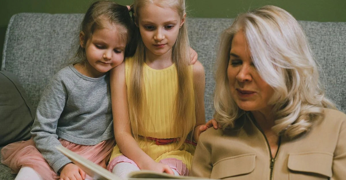 Une grand-mère aimante lit avec ses deux jeunes petites-filles à la maison, partageant un moment de complicité spécial.