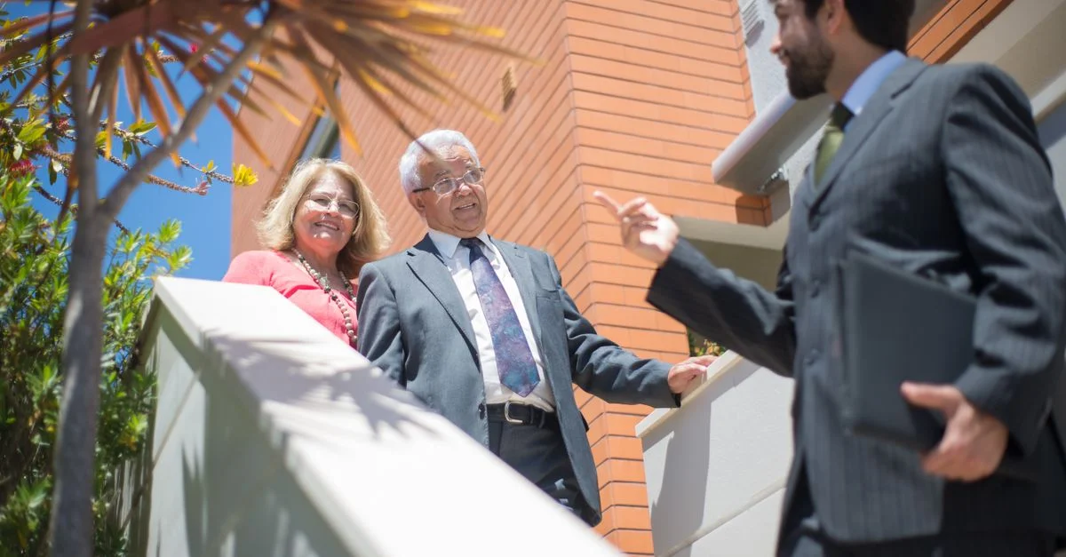 Couple âgé visitant une maison moderne avec un agent immobilier sous le soleil du Portugal.