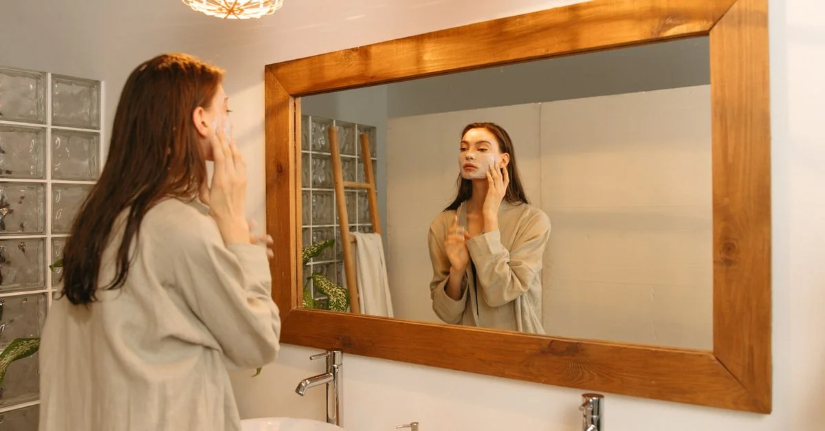 Femme appliquant une crème hydratante devant un miroir dans une salle de bain cozy.