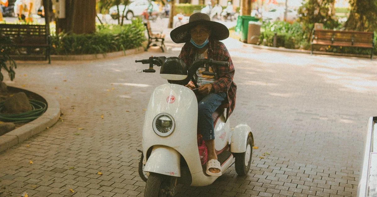 Une femme âgée circulant en scooter dans un parc de Hanoï, au Vietnam, portant un chapeau et un masque.