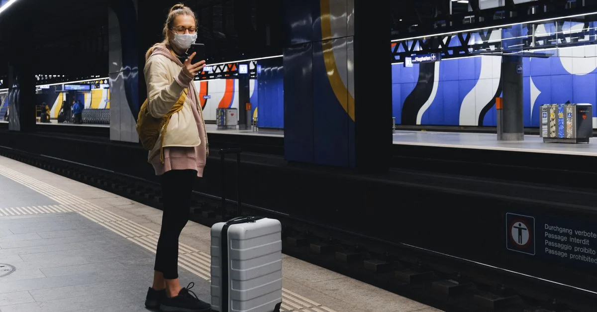 Une voyageuse portant un masque consulte son téléphone sur une plateforme de métro pendant la pandémie.