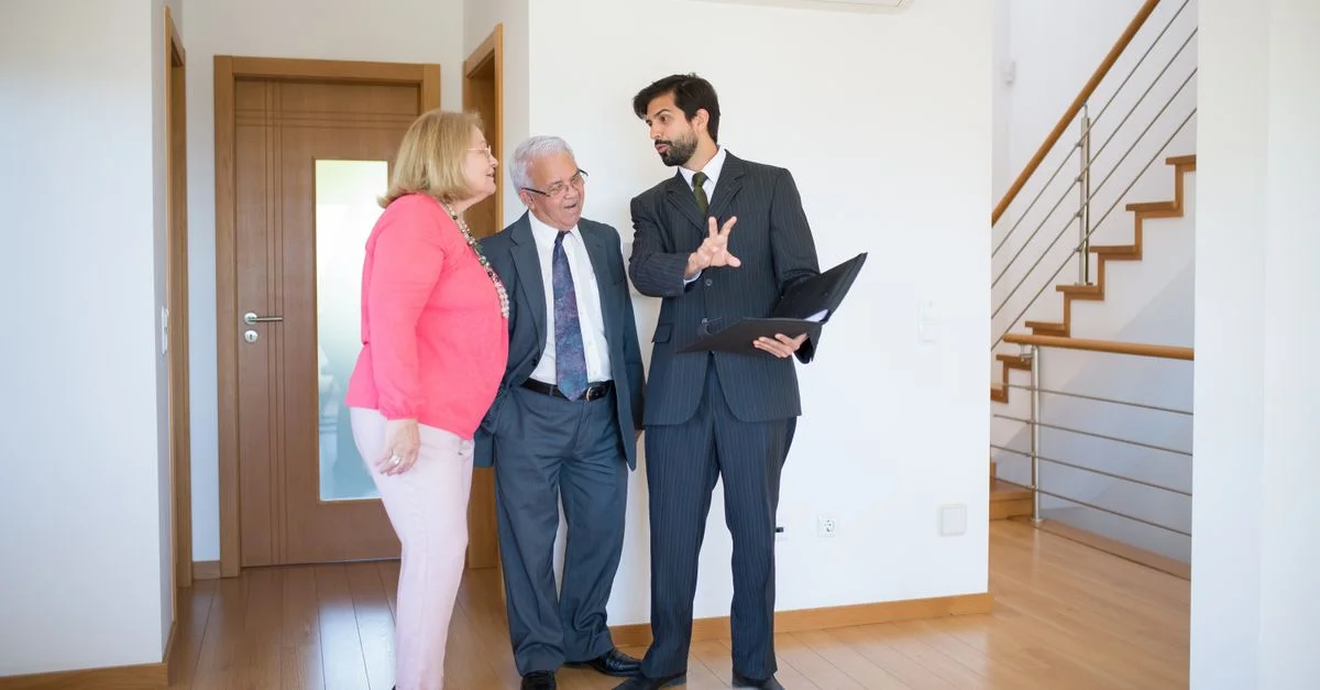 Agent immobilier montrant une propriété à un couple senior à l'intérieur d'une maison moderne au Portugal.