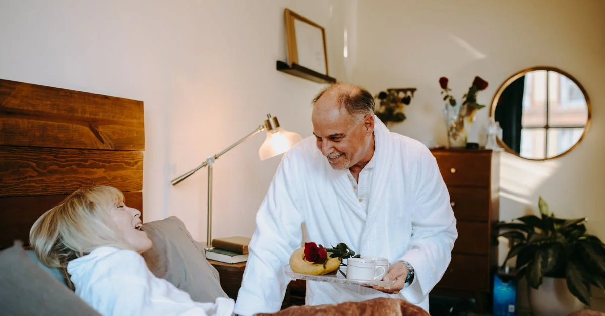 Un couple senior joyeux partageant un petit-déjeuner romantique au lit à la maison.