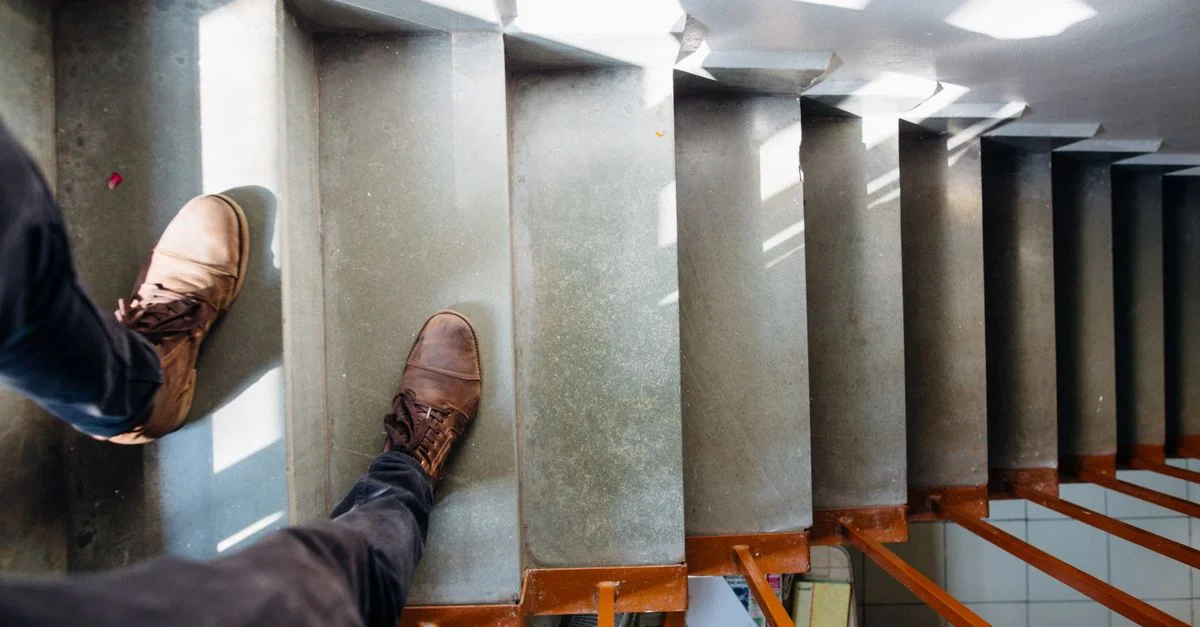 Vue de dessus d'une personne en chaussures en cuir descendant des escaliers bien éclairés à l'intérieur.