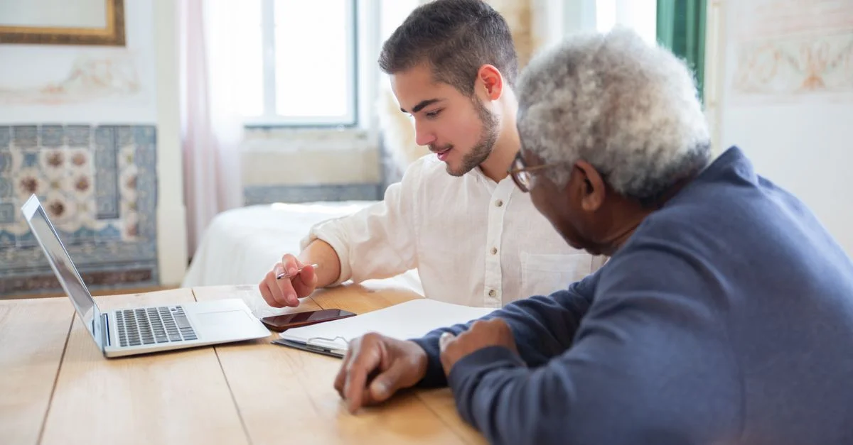 Jeune homme aidant un senior avec un ordinateur portable à la maison pour des besoins sociaux.