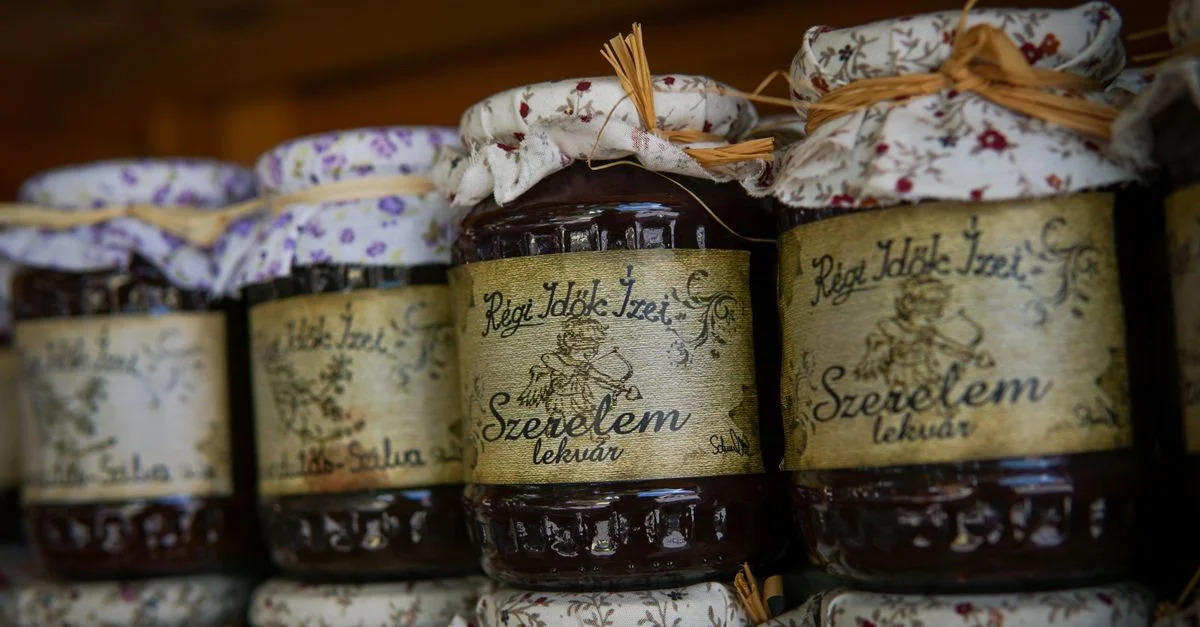 Gros plan de bocaux de confiture faits maison avec des couvercles en tissu floral et des étiquettes rustiques sur une étagère en bois.