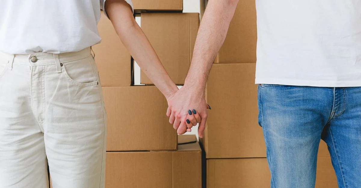 Un couple se tenant la main au milieu d'une pile de cartons de déménagement, symbolisant de nouveaux départs.