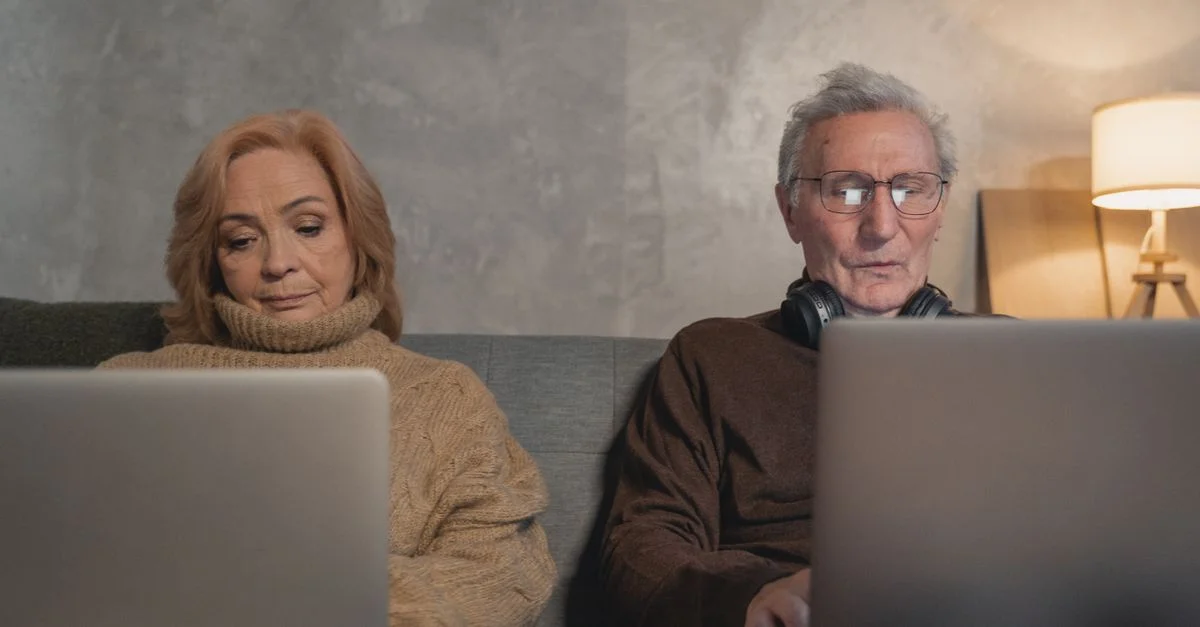 Couple âgé utilisant la technologie sur leurs ordinateurs portables à la maison, mettant en avant le mode de vie moderne des seniors.
