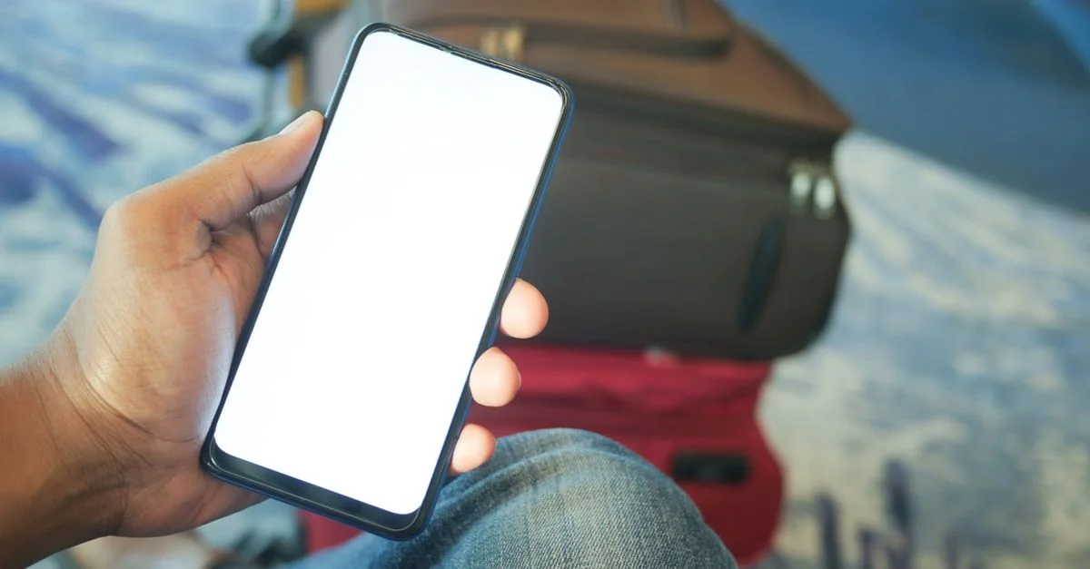 Une personne tenant un smartphone dans un aéroport avec des bagages visibles, idéal pour des concepts de voyage et de technologie.