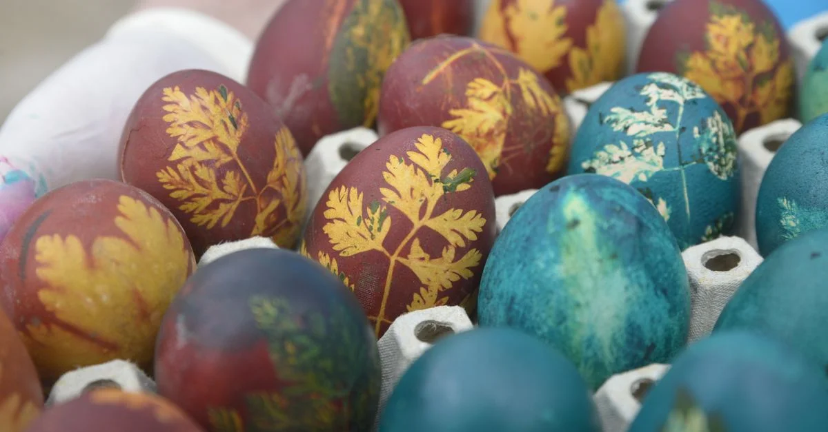 Des œufs de Pâques aux couleurs vives, décorés de motifs de feuilles, présentés dans un plateau en carton.